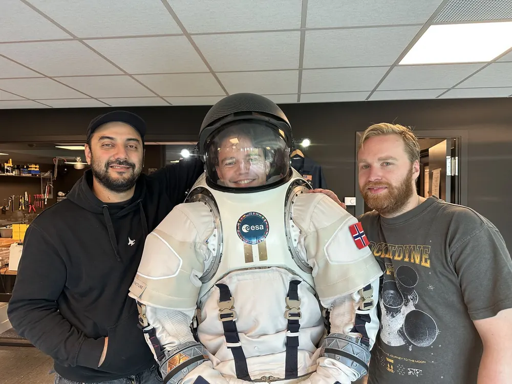 Freider i en hvit romdrakt med hjelm, mellom to folk fra Nåva Space